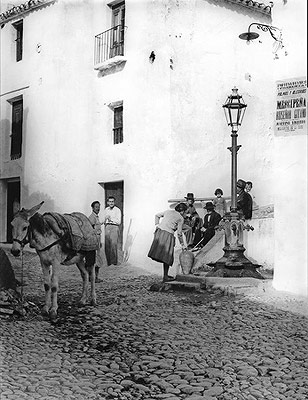 In a photo taken in the 60's, a woman collects water at a fountain using a clay receptacle and a mule to help her carry it home.