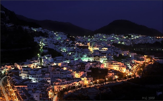A beautiful night shot of a glowing Frigiliana with the dark silhouette of the mountains in the background.